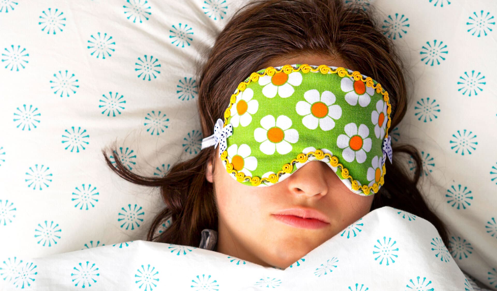 Eine Frau liegt auf einem Kissen, die Augen hinter einer geblümten Schlafmaske verborgen.