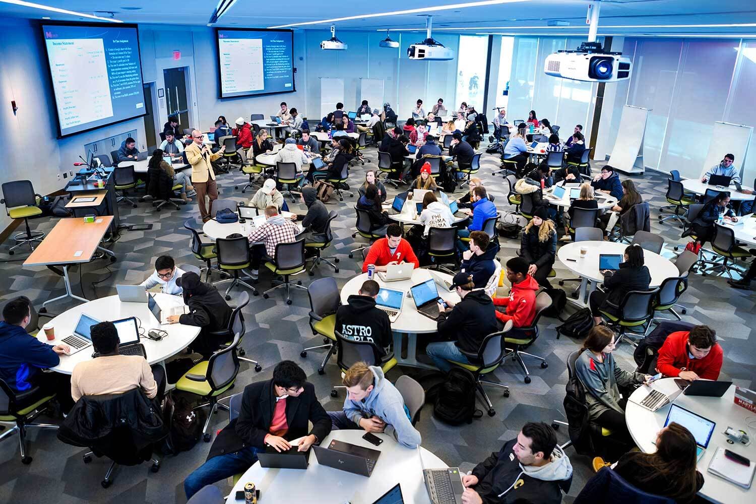View from above of a full classroom of students sitting at round tables.
