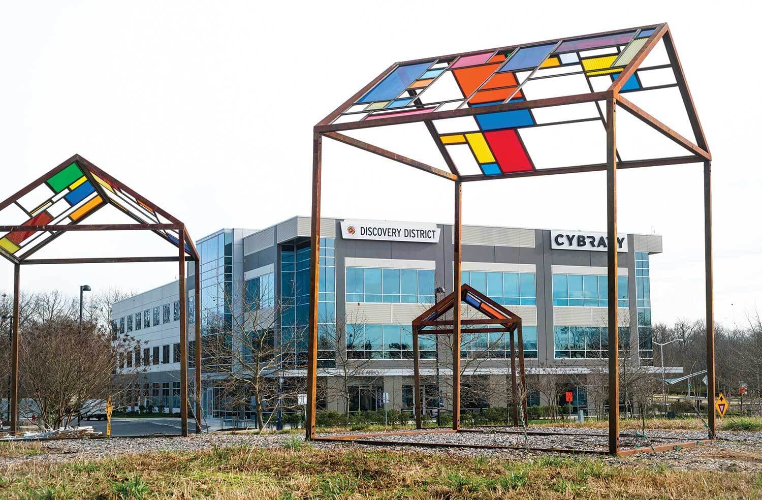 Several metal structures with clear glass on 3 sides and stained glass panels as the pitched roof. They stand outside in a grassy area.