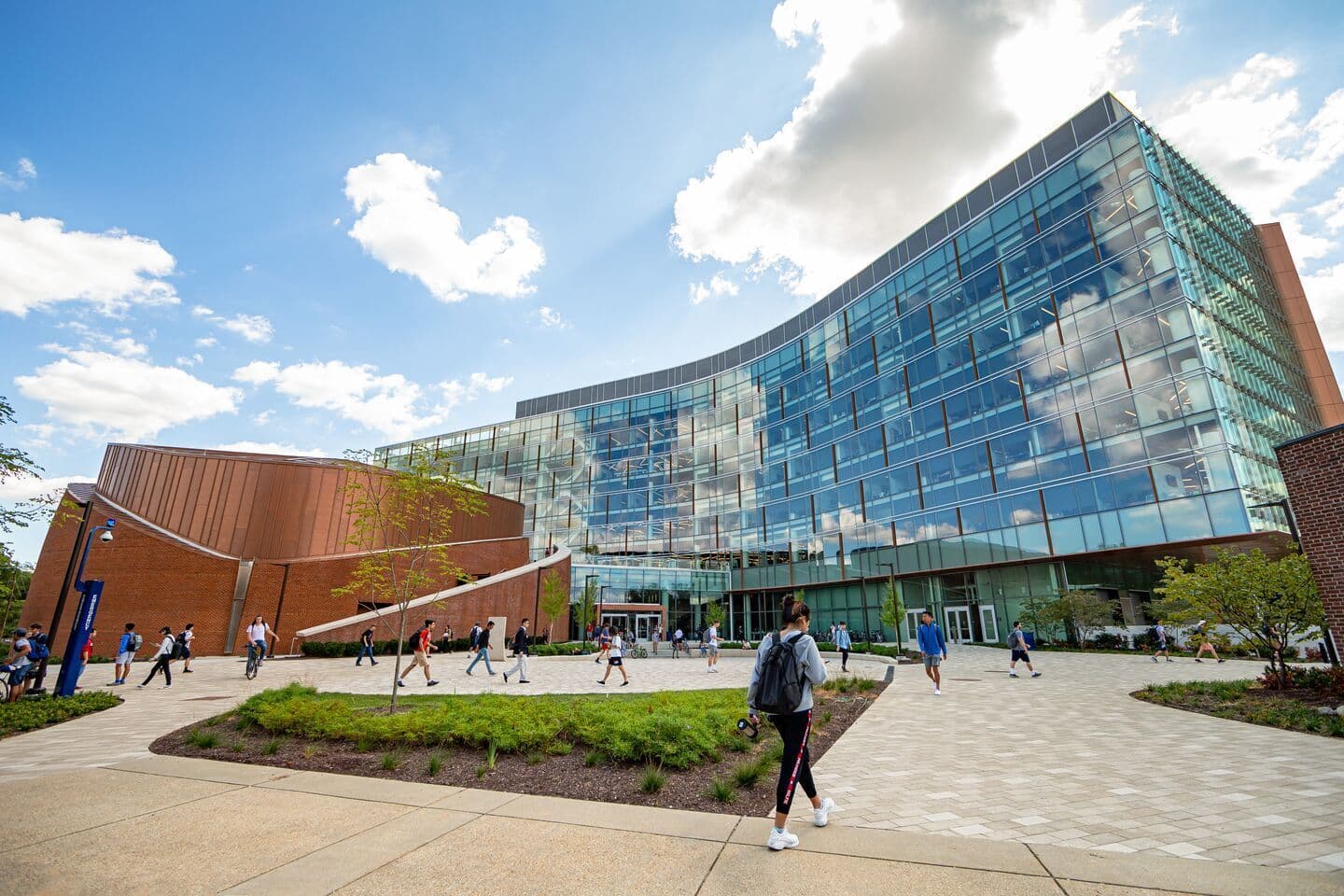Students walking in front of the Brendan Iribe Center building with blue sky reflecting in the building's many windows