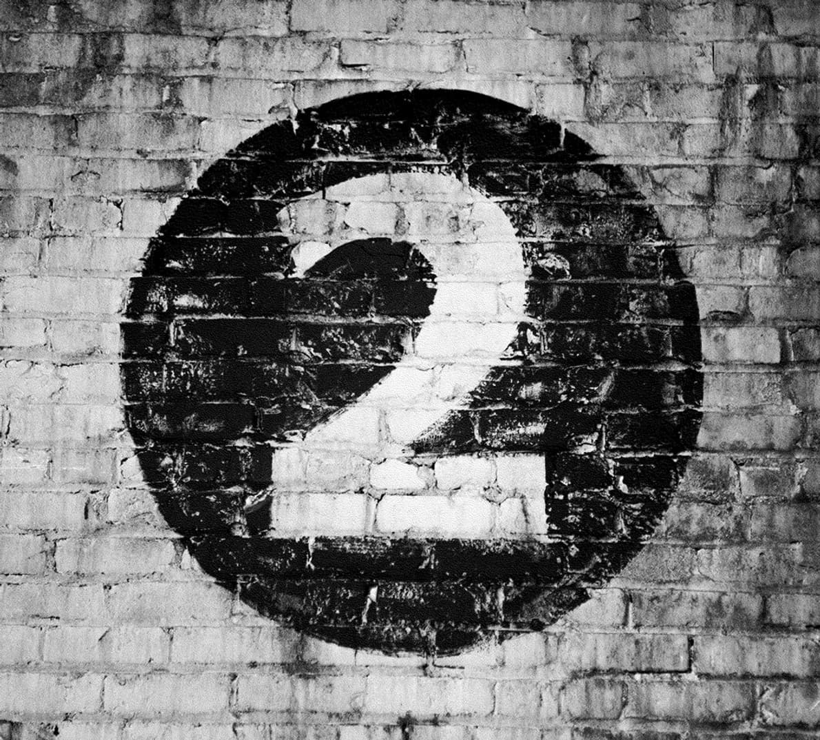 A white number '2' painted on a black circle on a brick wall.