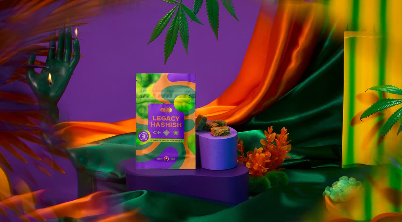A product shot of 'Legacy Hashish' in a scene with silk sheets, candles, and marijuana leaves.