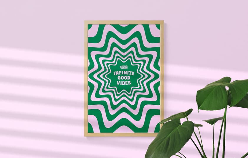 A poster that reads 'Infinite Good Vibes' in a wooden frame on a pink background with a plant in the bottom right corner.
