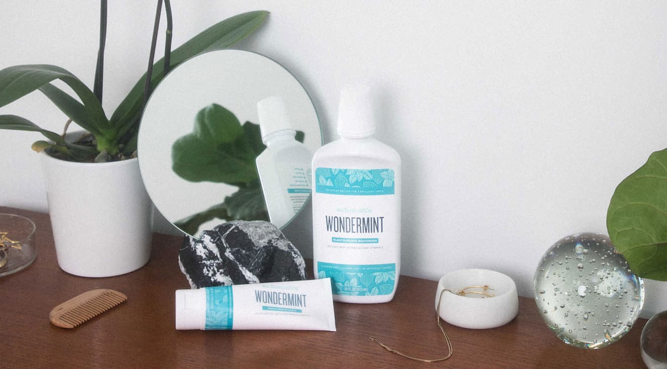A bottle of wondermint mouthwash and wondermint toothpaste sit on top of a table next to a plant and some other household items.