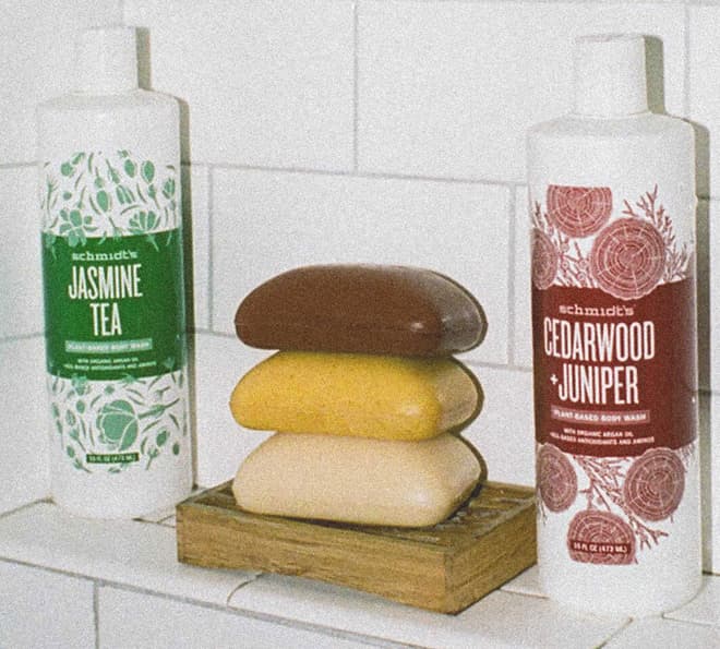 Jasmine tea and cedarwood+juniper scented body wash bottles on a shower shelf with bars of soap stacked in the middle.