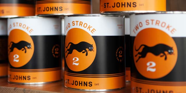 Coffee cans are stacked on top of each other with the Two Stroke logo on them.
