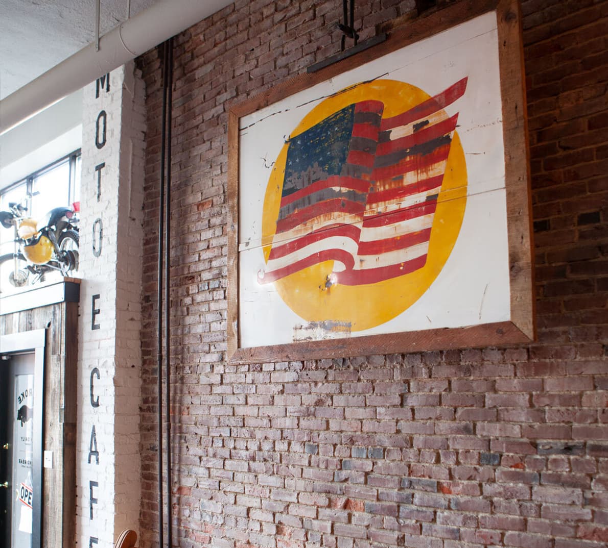 An interior shot of the Two Stroke Coffee shop shows a framed painting of an American flag on a red brick wall.