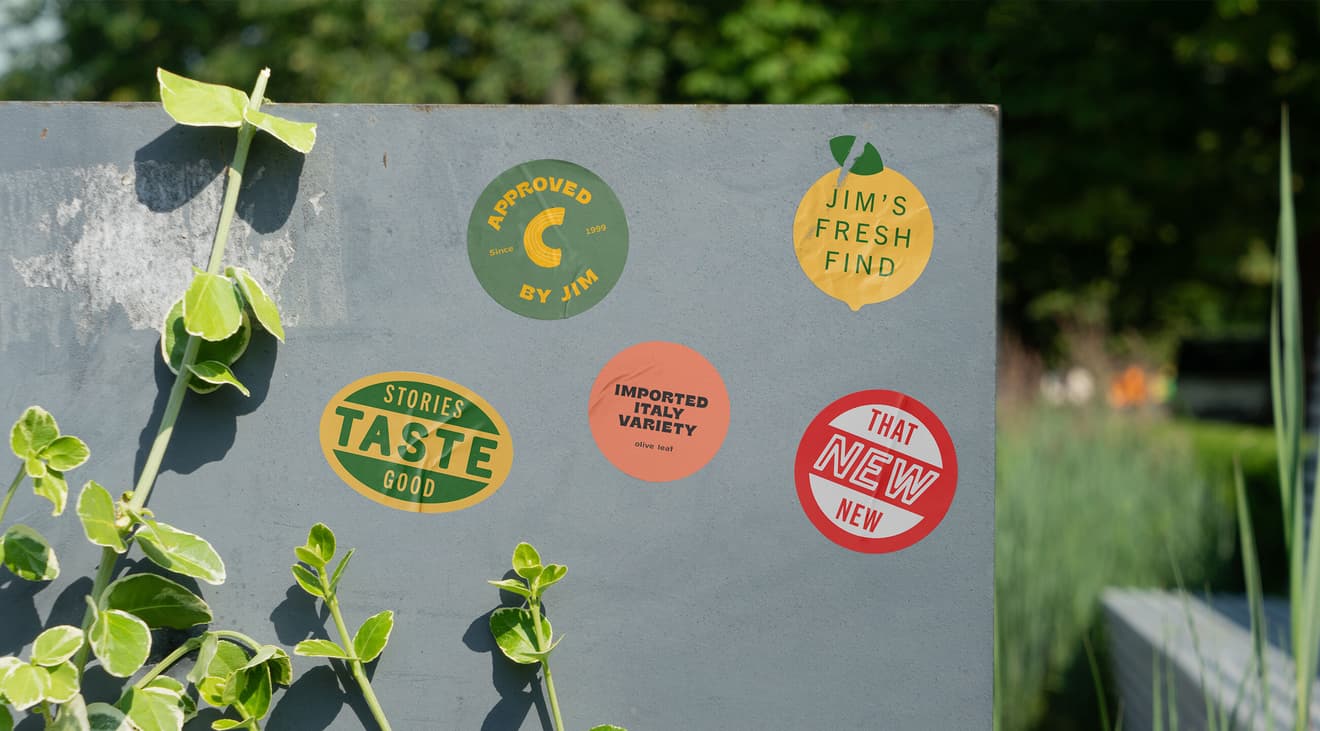 Various Wellspent Market stickers on the side of a wall next to a plant. 