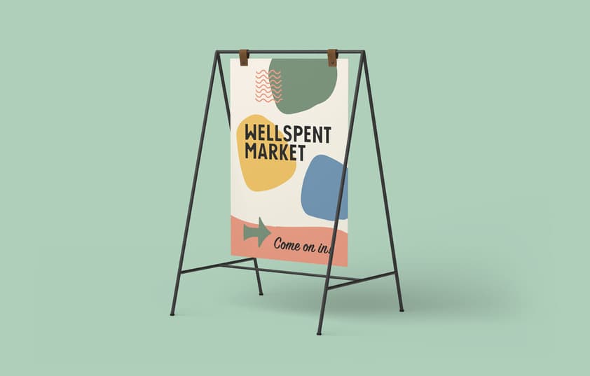 An A-frame sign with the Wellspent Market logo on it with various shapes and patterns.