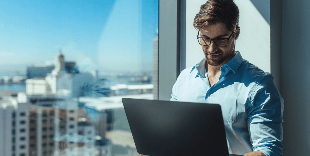 Man looking at a laptop in front of a window