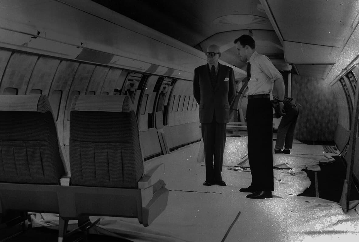 Walter Dorwin Teague standing in an airplane mockup with a designer