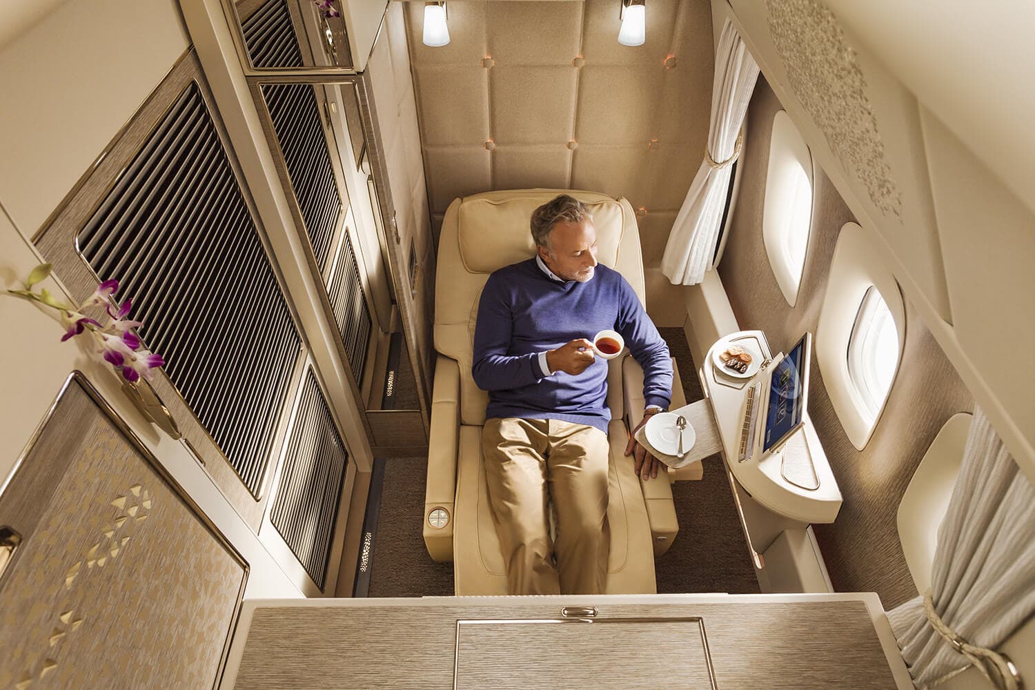 Emirates cream and gold First Class cabin suite interior with man seated drinking tea