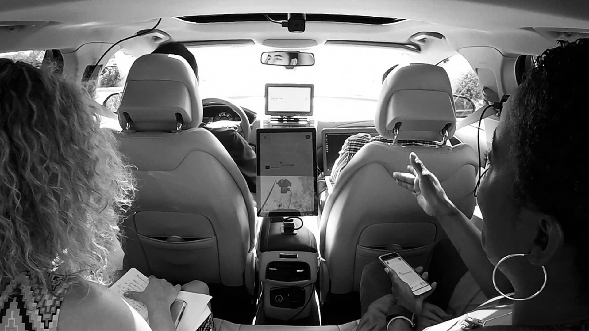 Three people sitting in car with phones and clipboards conducting user research