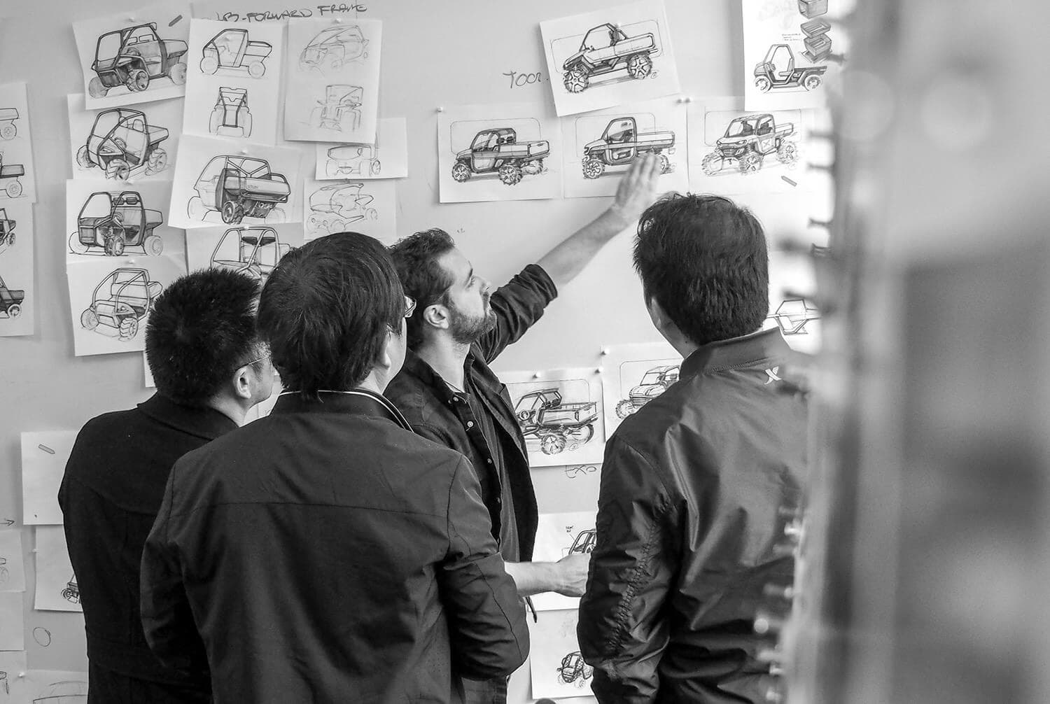 Four men standing in front of white board reviewing sketches of vehicles