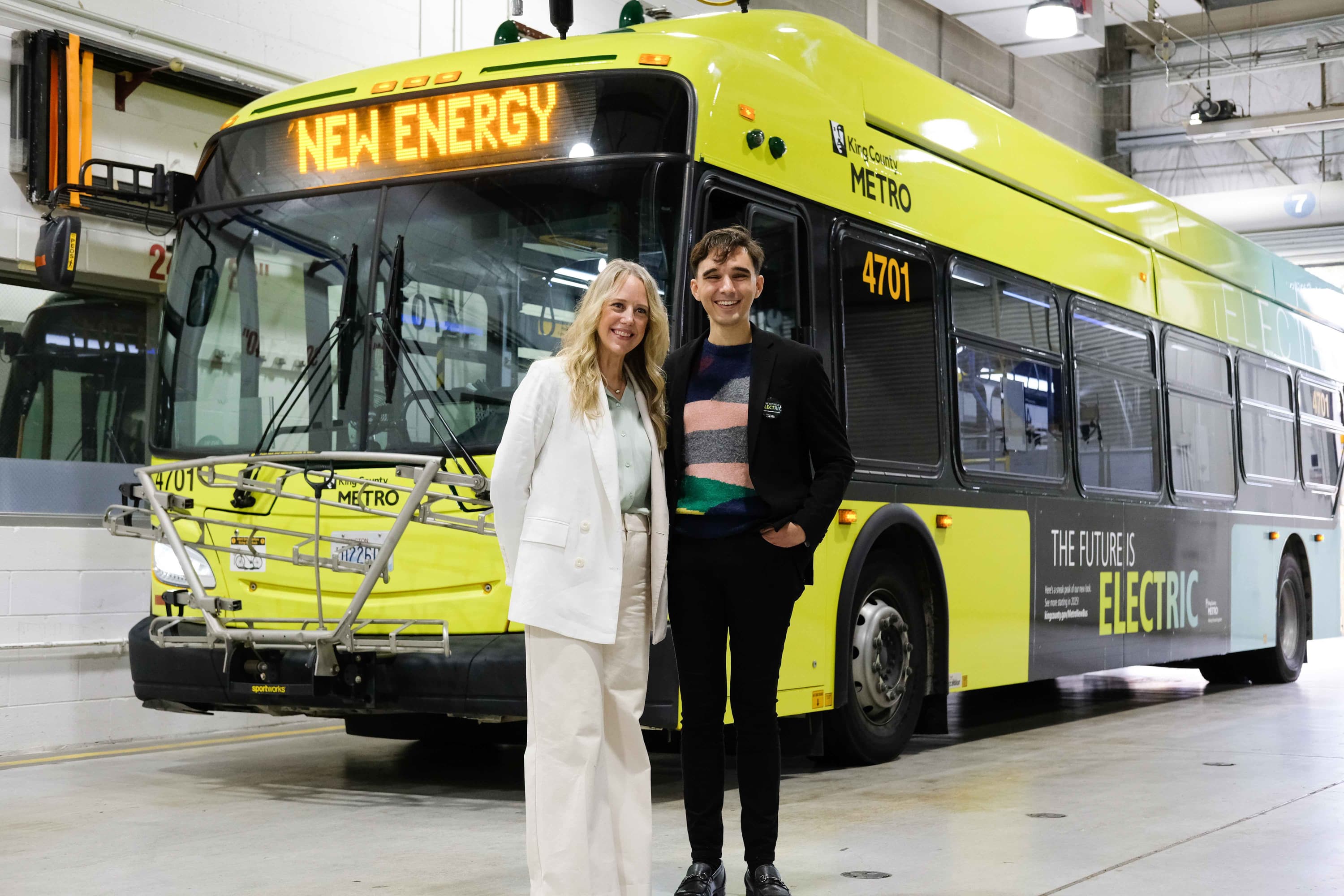 Katie Ryan and Anthony Harding, part of the Teague team that designed the new livery for King County Metro, stand in front of the yellow city bus.