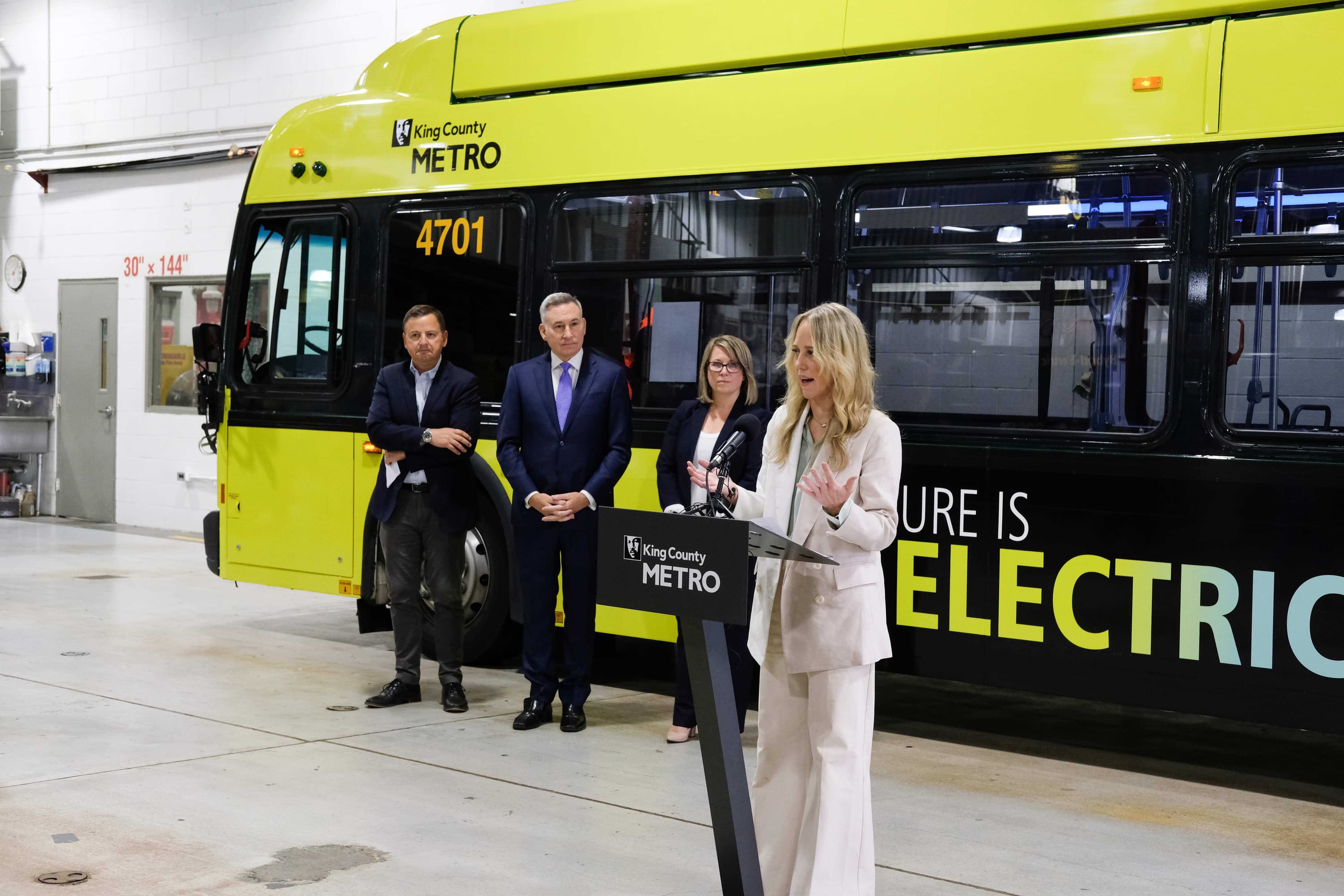 Katie Ryan, livery design manager from Teague, speaks at a press conference with Dow Constantine about the new designs for the King County Metro bus, which is behind her.