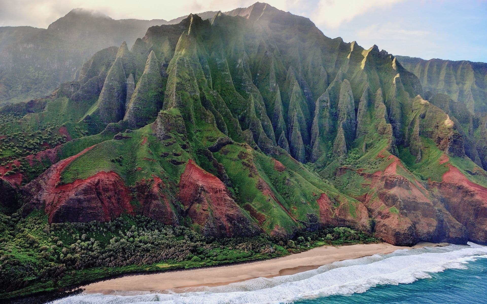 Coastline of Hawaii with mountains in the background and crystal blue waves hitting the beach