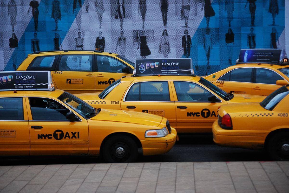 NYC taxi cabs lined up on the street in front of a blue wall