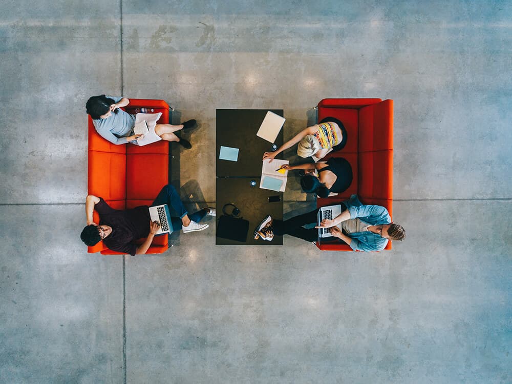 Aerial photo of people collaborating with red sofa and concrete floors