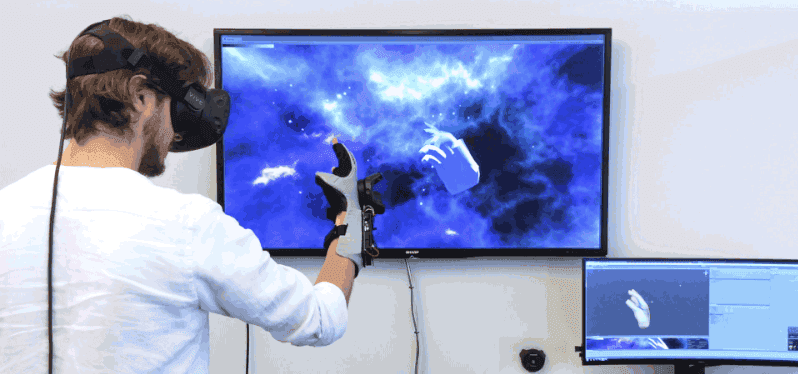 Man in VR goggles standing in front of computer monitors with Nintendo power glove on