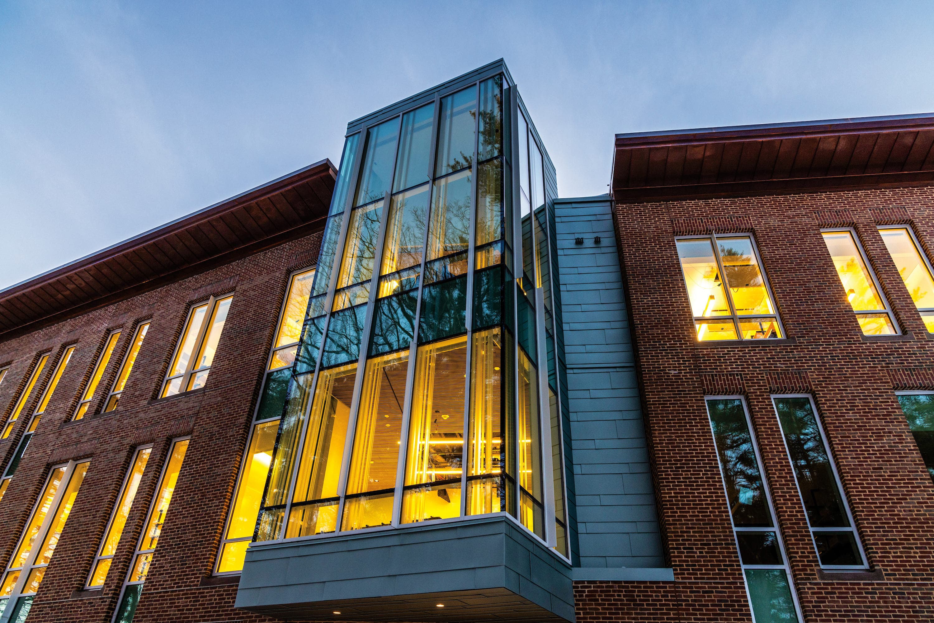 Warm light illuminates the windows from the inside of the Class of 1982 Engineering and Computer Science Center at dusk.