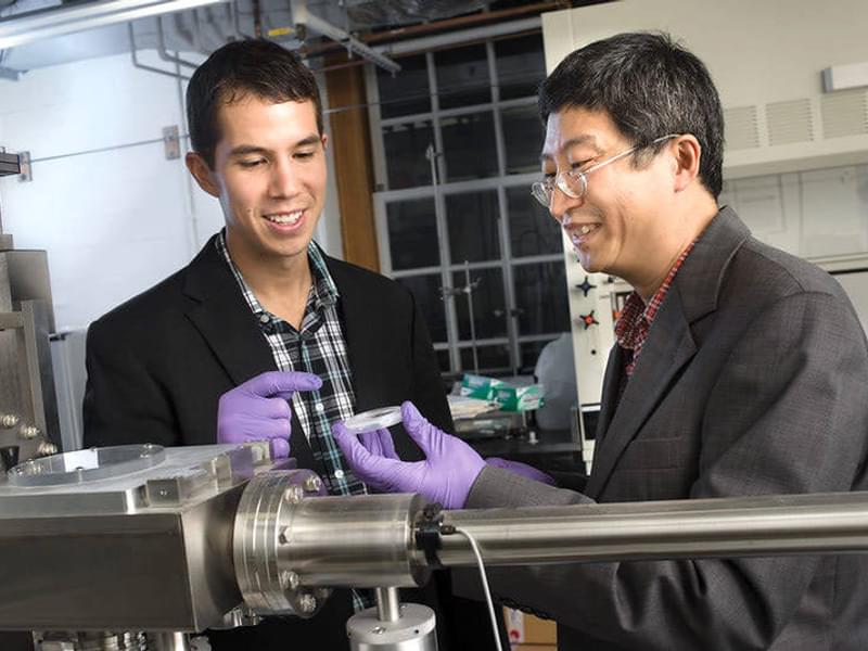 A student works with Professor Jifeng Liu in his lab with large equipment and a sample in a small ish