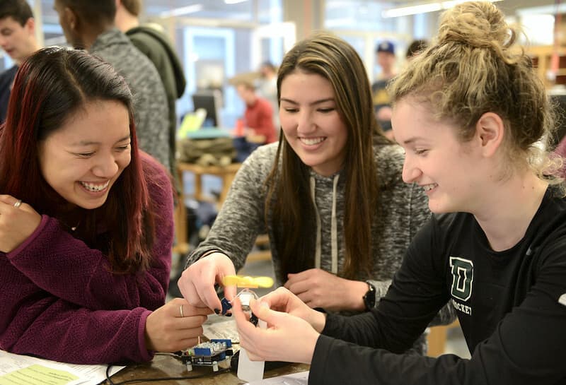 Three smiling female engineering students work on a motor project in intro to engineering class.