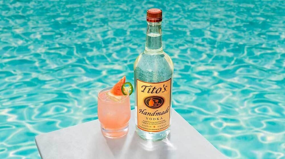 Tito's Spicy Watermelon cocktail and Tito's Handmade Vodka bottle by a swimming pool