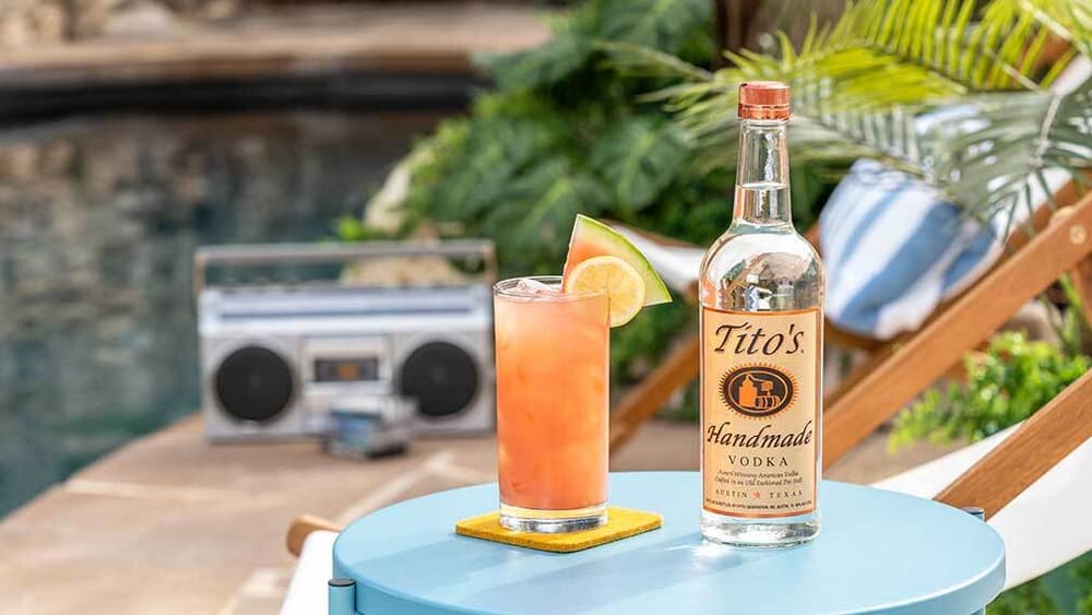 Tito's Summertime Sparkler next to a Tito's Handmade Vodka bottle by a swimming pool