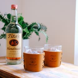 Leather Highball Set with Tito's Handmade Vodka logo on a table with a bottle of Tito's