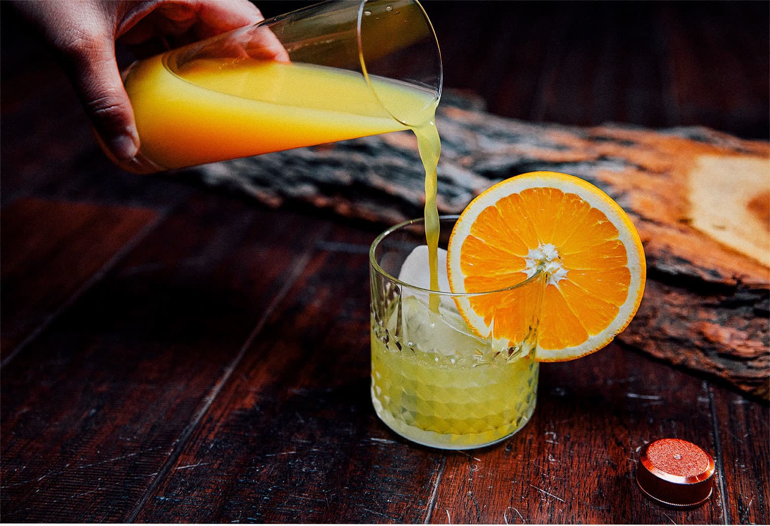 Orange juice being poured in a rocks glass garnished with an orange slice