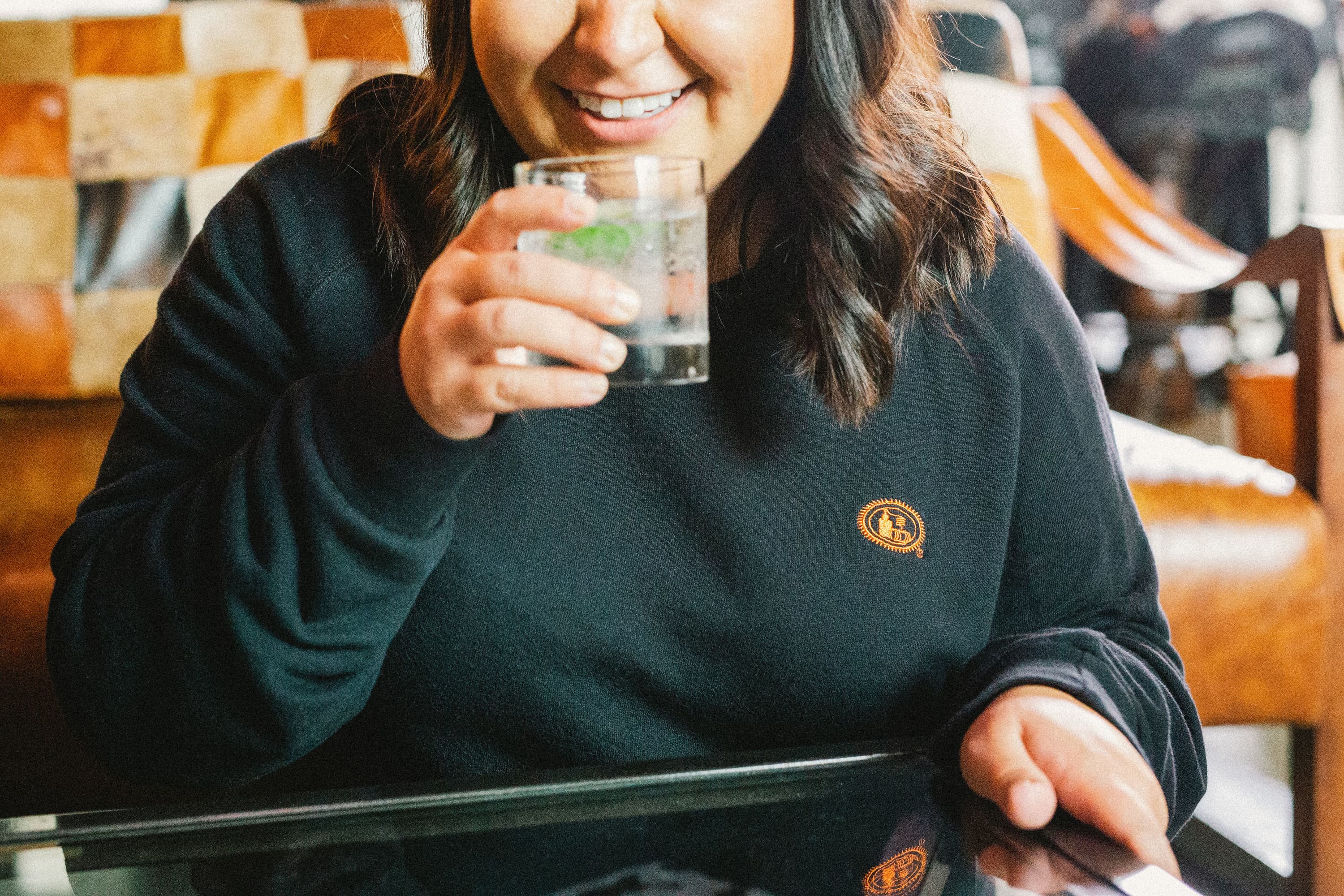 Girl holding a Tito's cocktail in a rocks glass wearing our black pullover with potstill emblem on the right chest