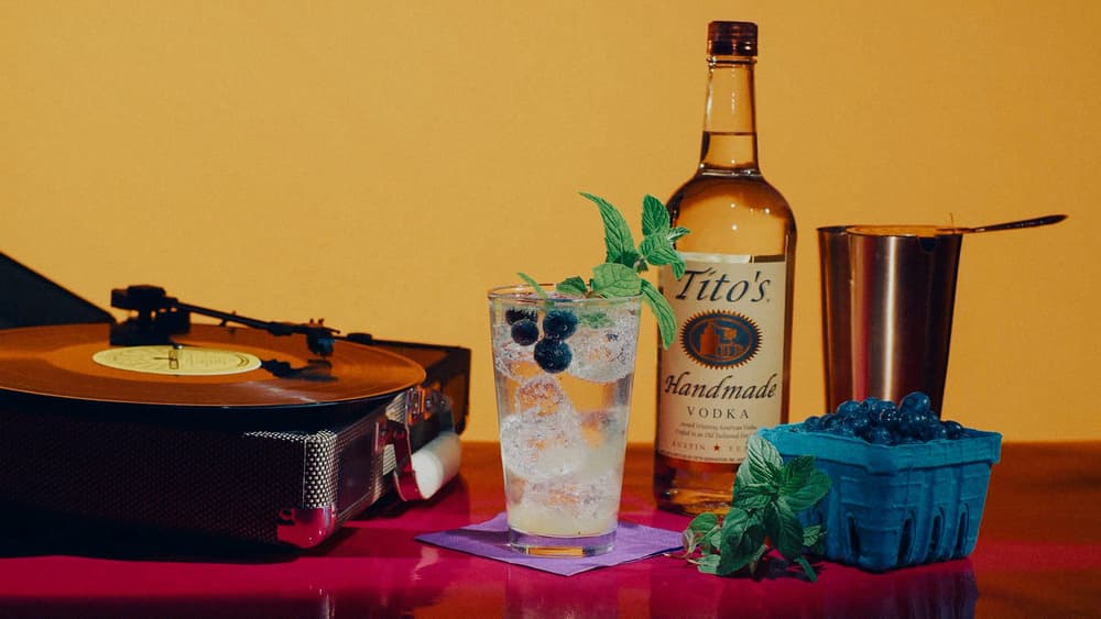 Tito's Smash Hit cocktail garnished with mint and blueberries, a Tito's Vodka bottle, and a record player