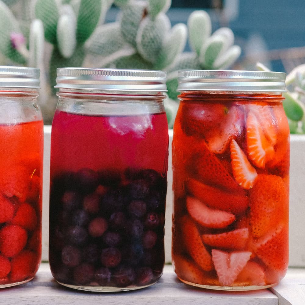Three mason jars filled with Tito's Vodka, raspberries, blueberries, and strawberries