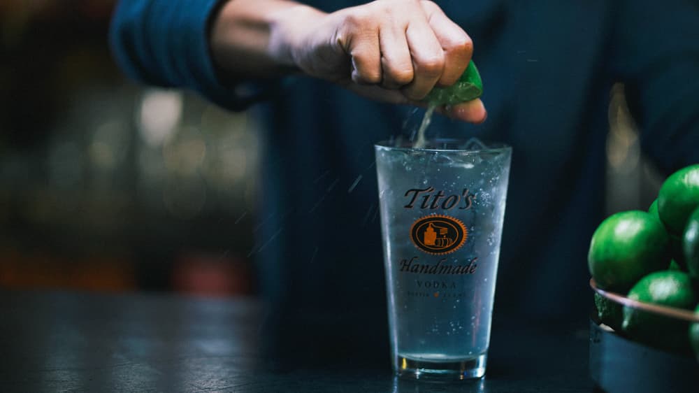 Tito's Buzzer Beater in pint glass on bar top with man squeezing lime