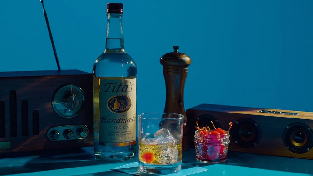 Tito's Cigar Box cocktail garnished with a maraschino cherry, a Tito's Vodka bottle, and two vintage radios