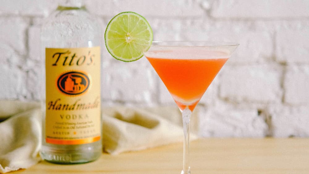 Tito's Vodka bottle next to a cosmo in a martini glass