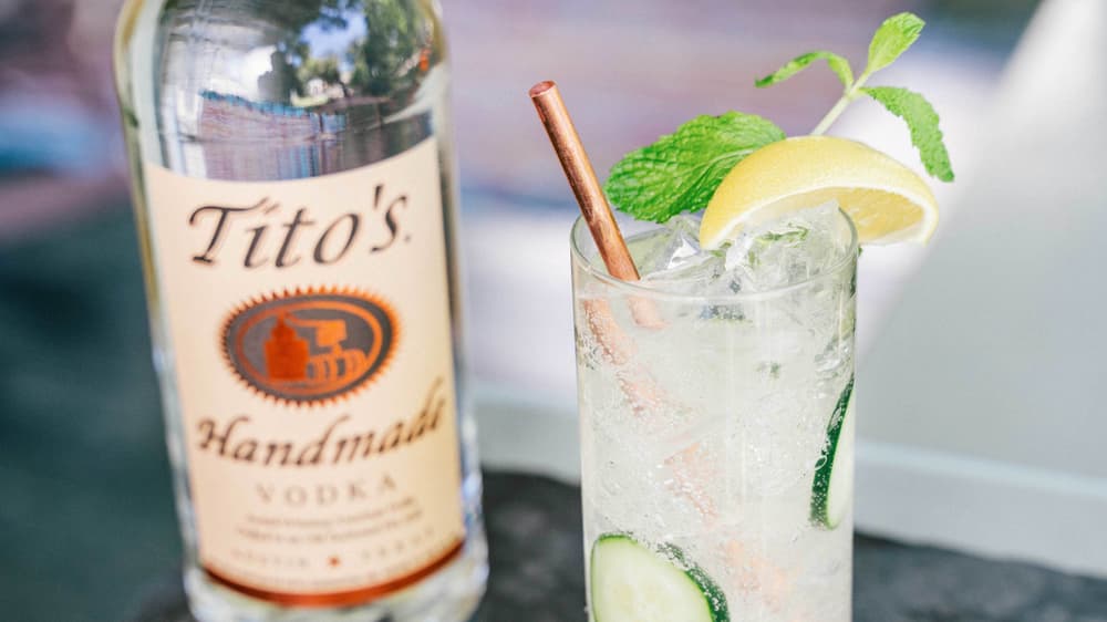 Tito's Cucumber Collins cocktail next to a Tito's Vodka bottle