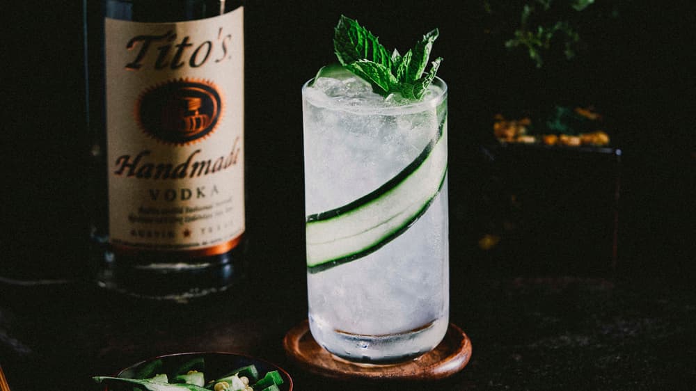 Tito's Cucumber Mint Cooler in a tall glass next to a Tito's Vodka bottle