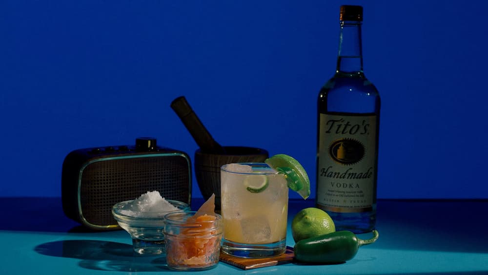 Tito's Fire Killer cocktail garnished with lime and jalapeno, a bottle of Tito's Vodka, and a vintage radio