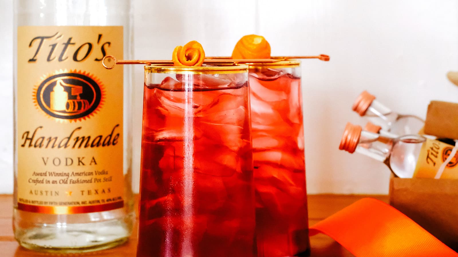 Tito's Vodka bottle and two Tito's for Two cocktails on a table next to an orange and Tito's mini bottles