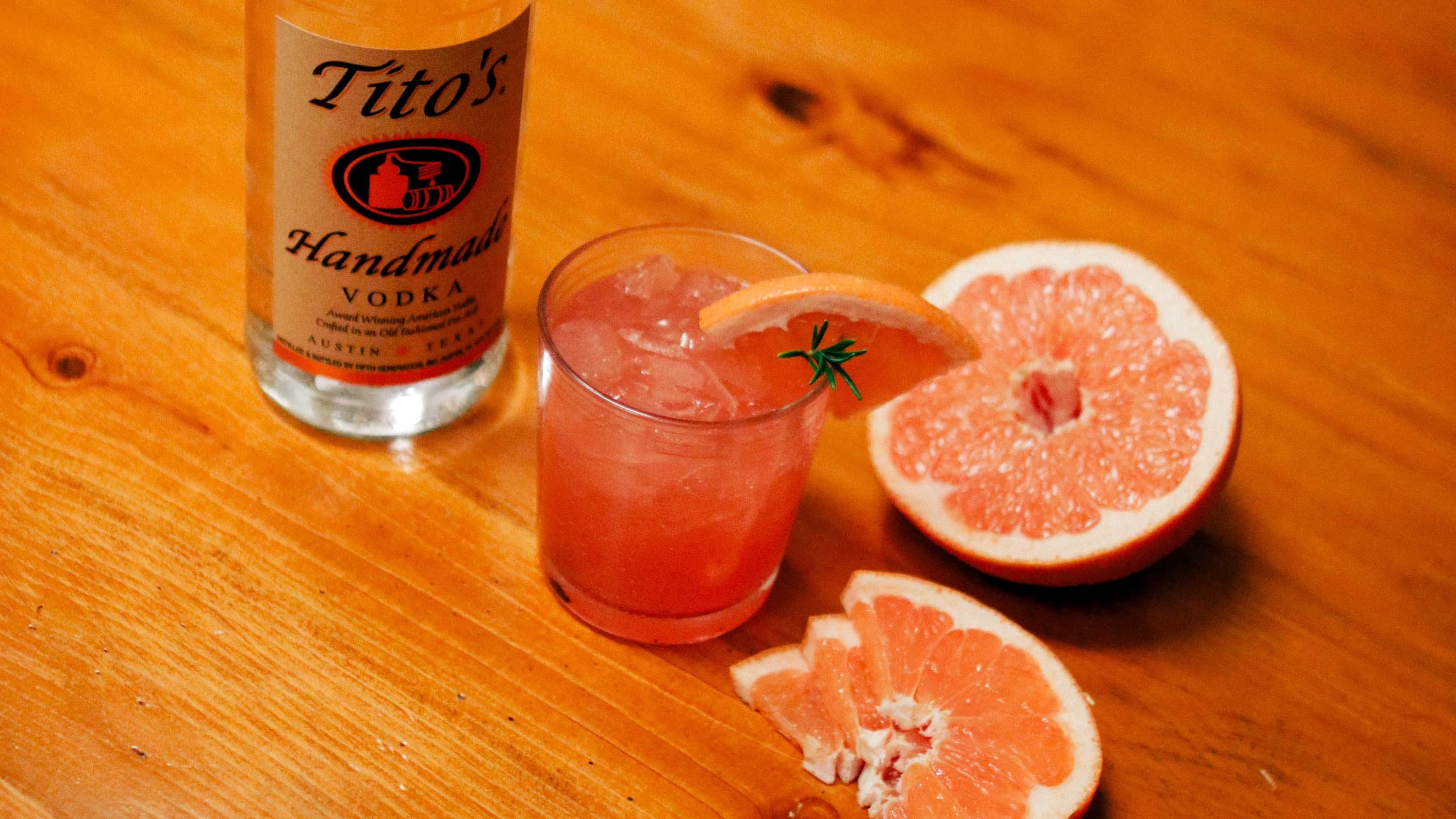 Tito's Vodka bottle next to a Tito's Greyhound garnished with a grapefruit slice