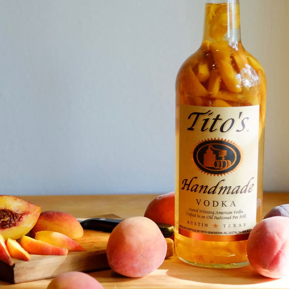 Tito's Handmade Vodka bottle on a cutting board with peaches