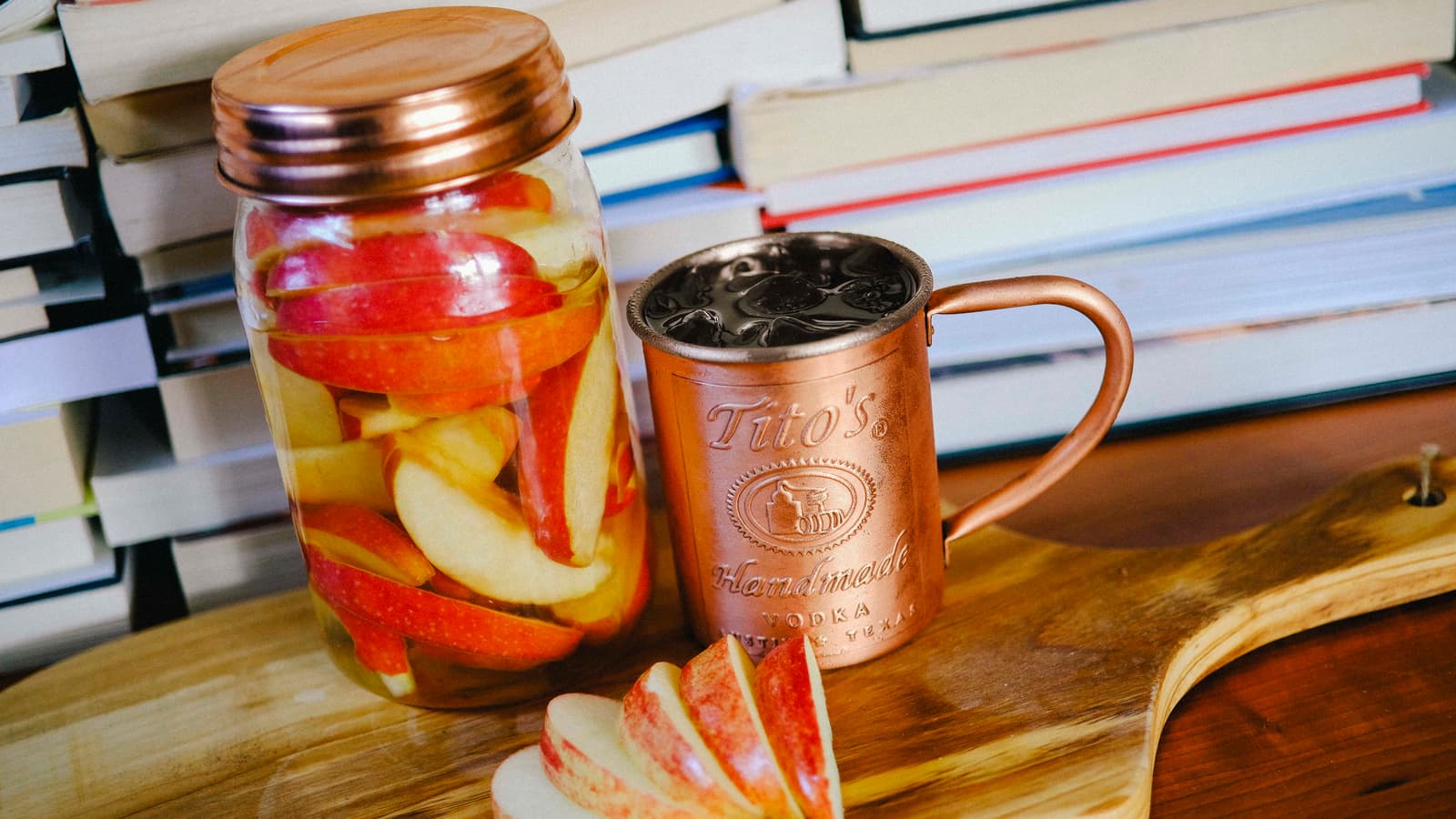 Mason jar filled with apples and Tito's Vodka next to a copper mug