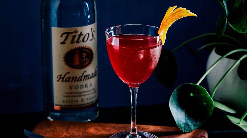 Tito's Red Lotus in a martini glass next to a Tito's Vodka bottle