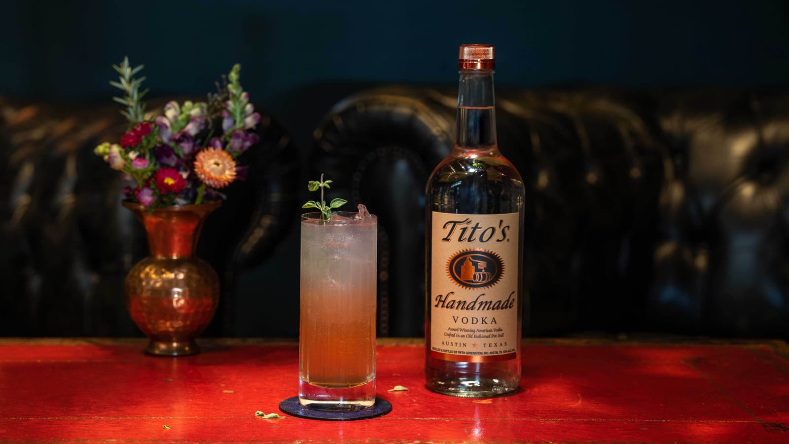 Tito's Pom Spritz on a table with a Tito's Handmade Vodka bottle and flowers
