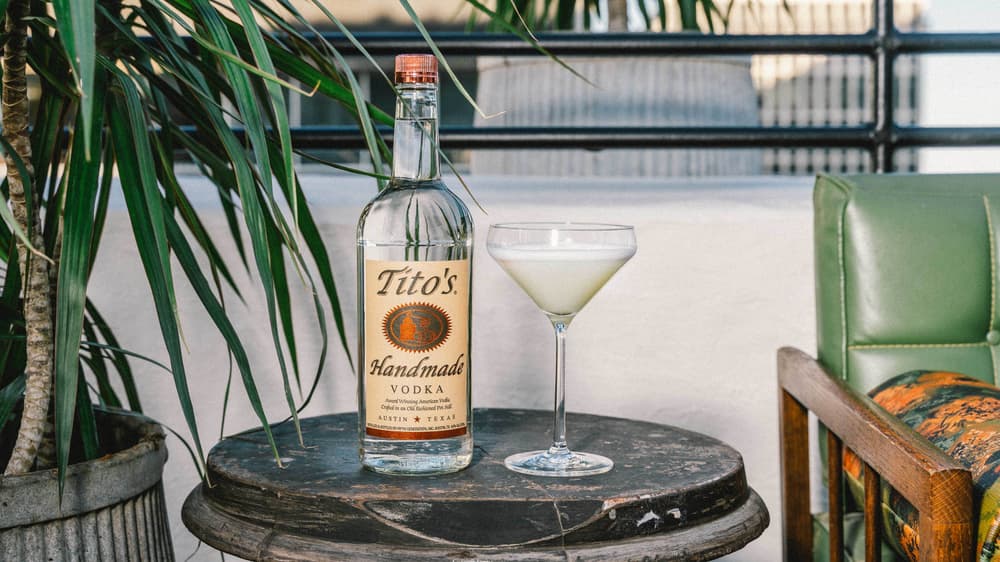 Tito's Sour Cocktail next to a bottle of Tito's Vodka on a table