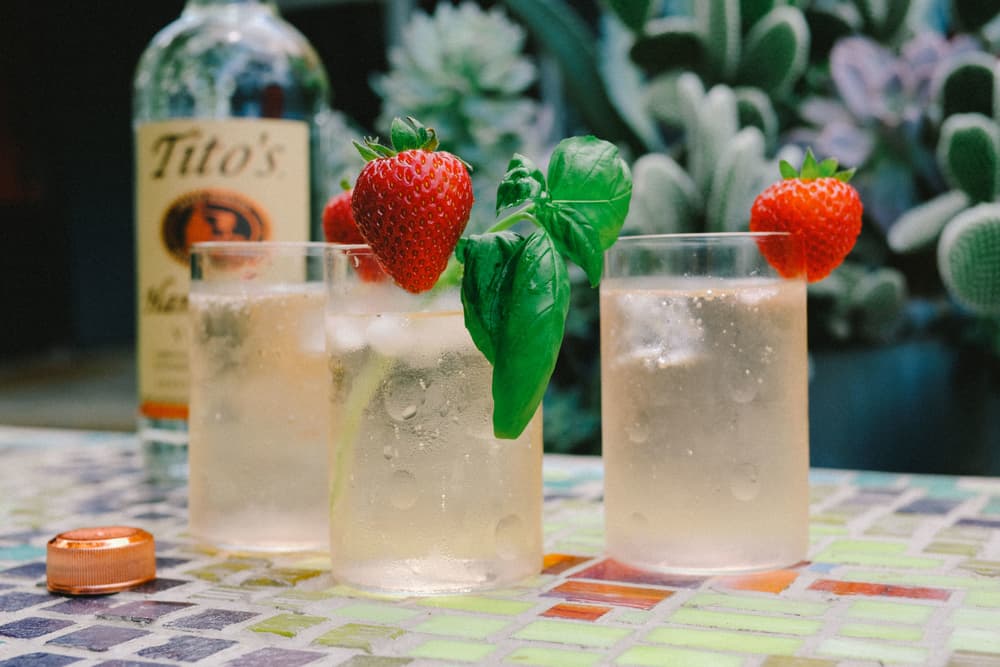 Three Tito's Strawberry Bazil Spritzer cocktails with a Tito's Vodka bottle in the background