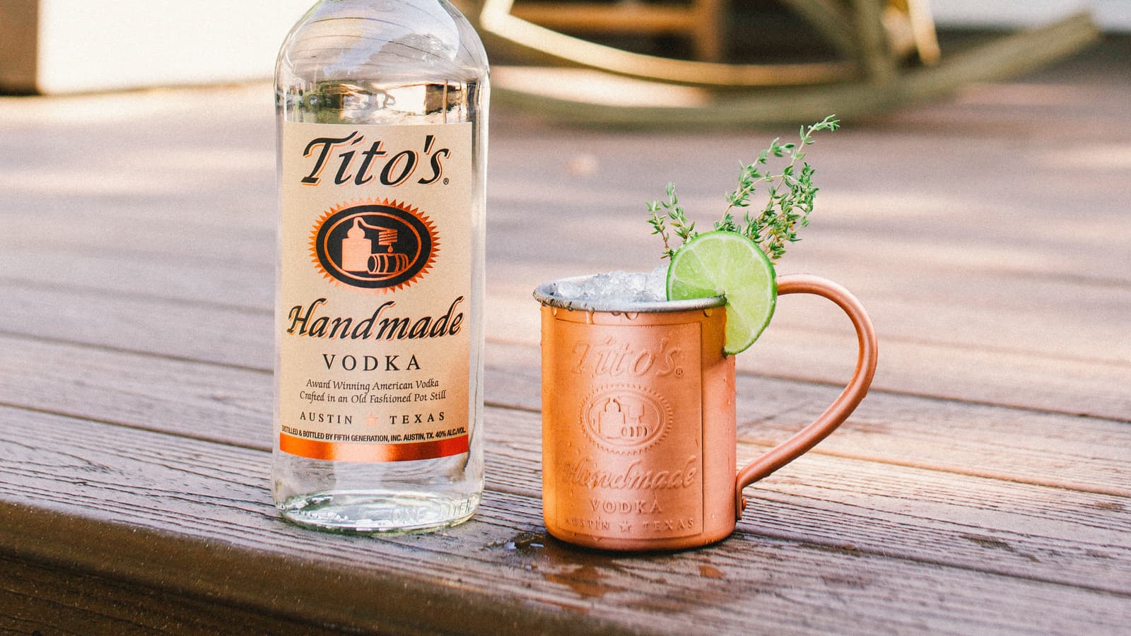 Tito's bottle next to Tito's Thyme Out in a Tito's Copper Mug on a porch with a rocking chair in the background