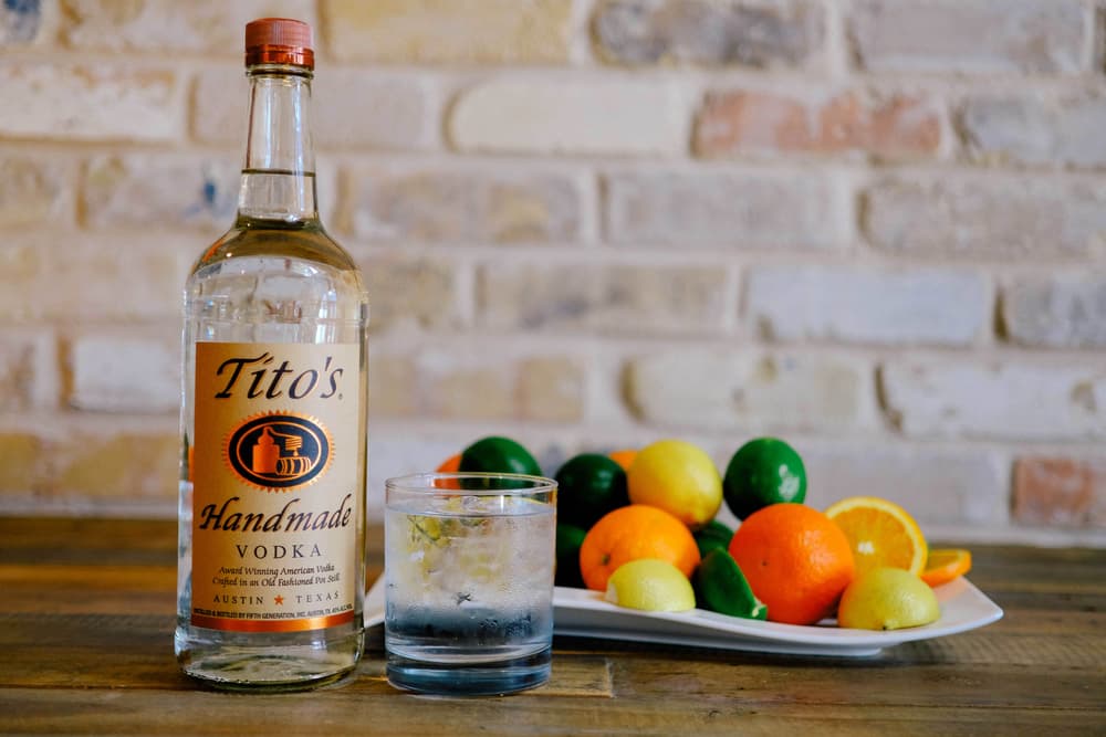 Tito's Vodka bottle next to a Tito's & Tonic cocktail with a plate of citrus fruits
